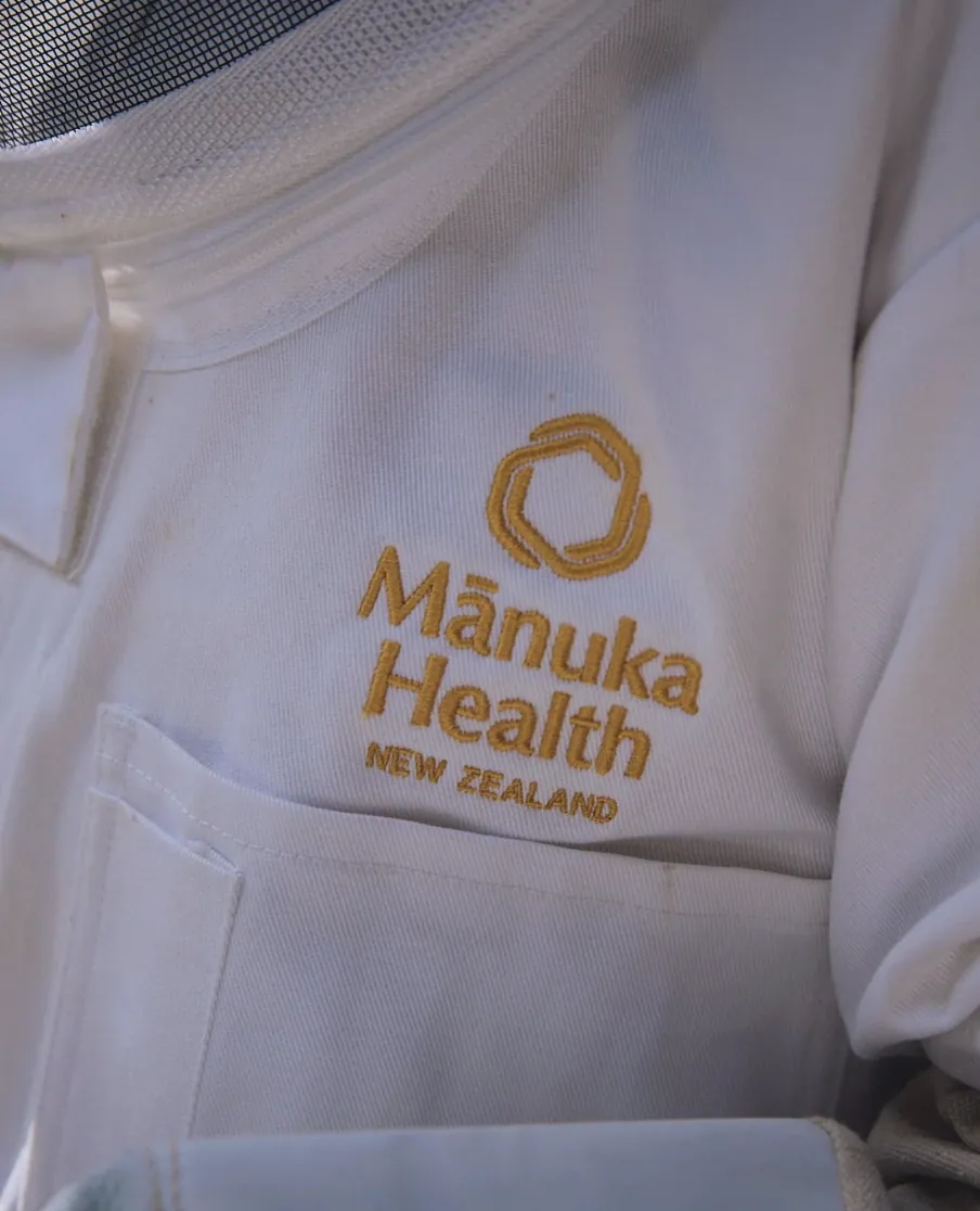 Gold Mānuka Health New Zealand embroidery on a white beekeeper suit