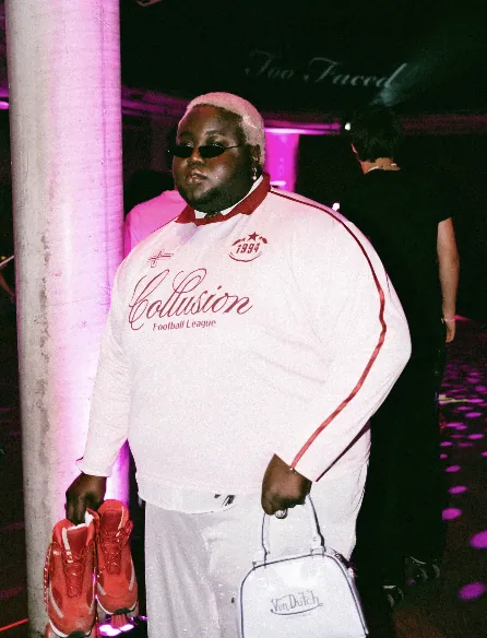 Guest in a white Collusion jersey holding red roller skates beneath the too faced neon sign
