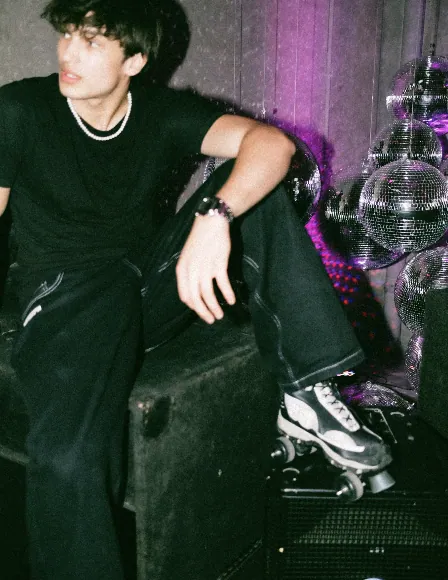 Guest in black with pearls resting between roller skates and a wall of disco balls