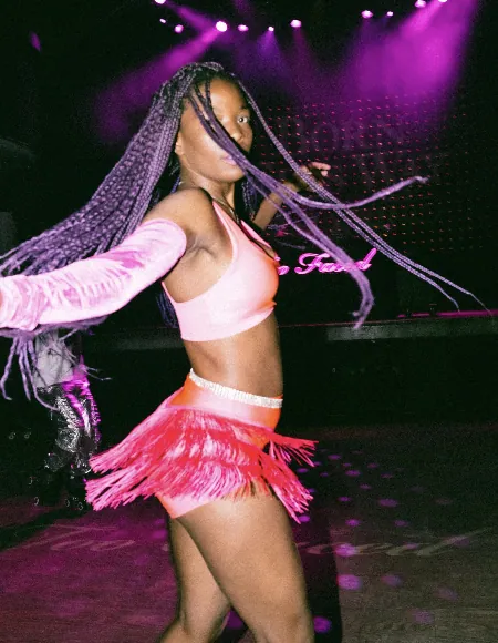 Performer with long braids dancing in a pink fringed outfit under magenta stage lights