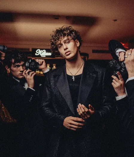 Guest in black tailoring surrounded by photographers at the Kilian PARIS event