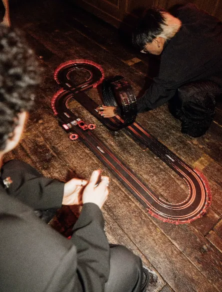 Guests racing miniature cars around a red and black track on the wooden floor