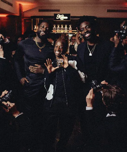 Three guests smiling amid photographers at the Kilian PARIS nightlife event