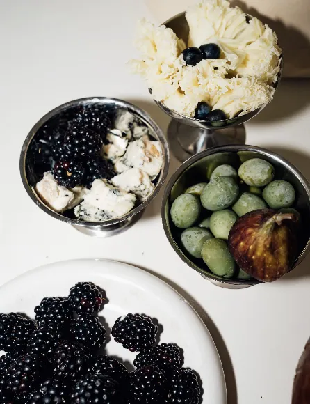 Silver bowls with blackberries, cheese, olives and edible flowers