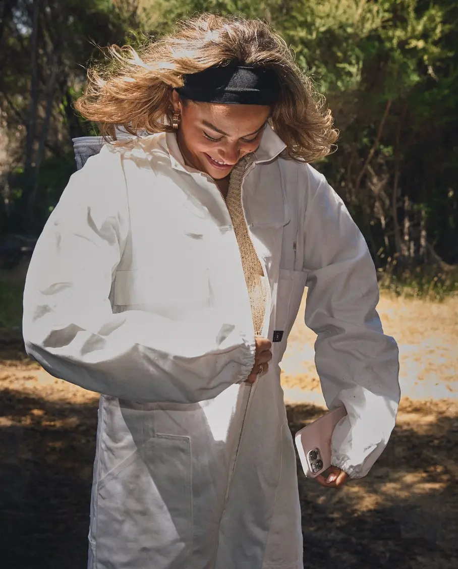 Guest zipping up a white beekeeper suit outdoors