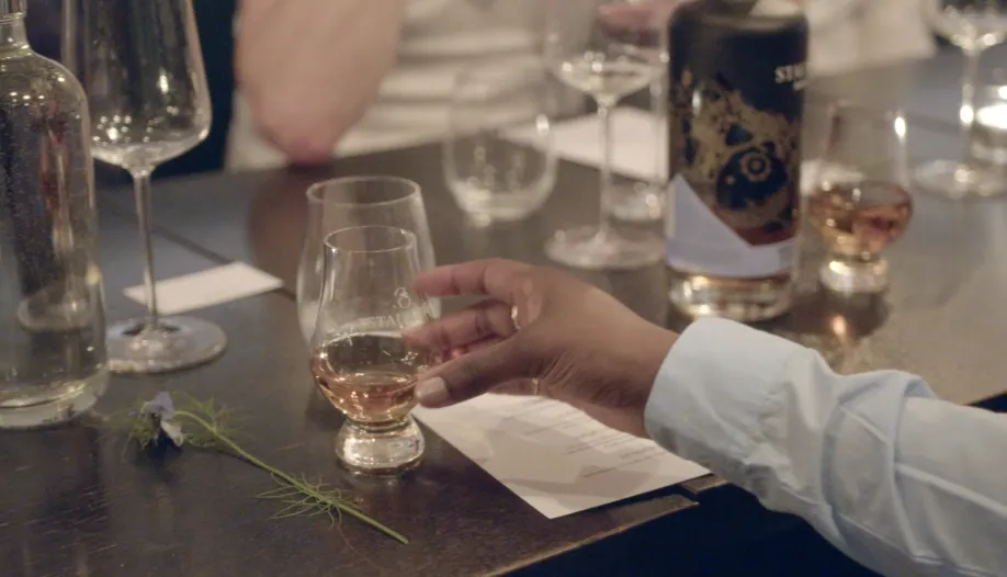 Hand reaching for a STAUNING tasting glass beside the høst bottle