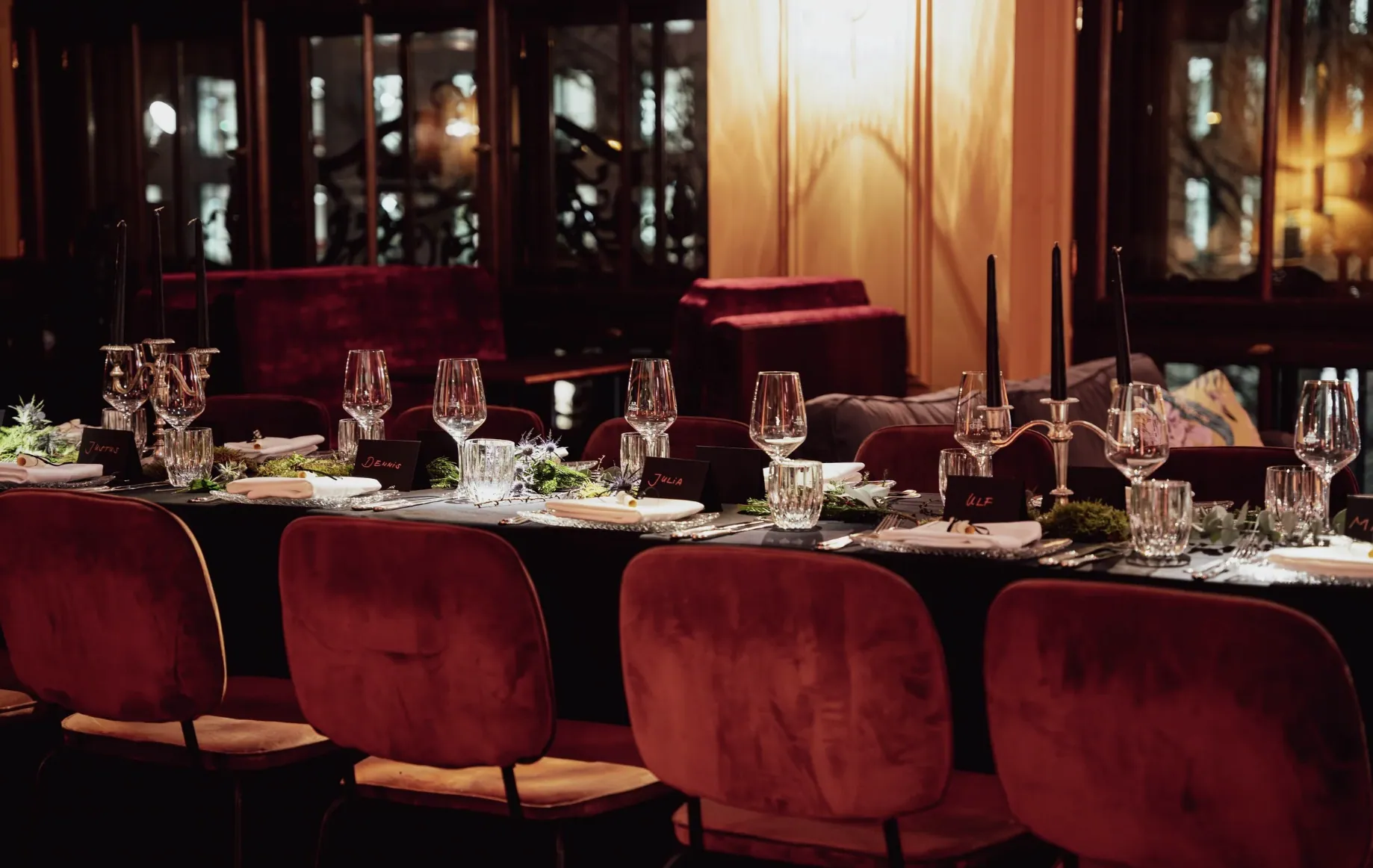 A long dinner table in deep red velvet and candlelight, set with crystal glasses and handwritten place cards