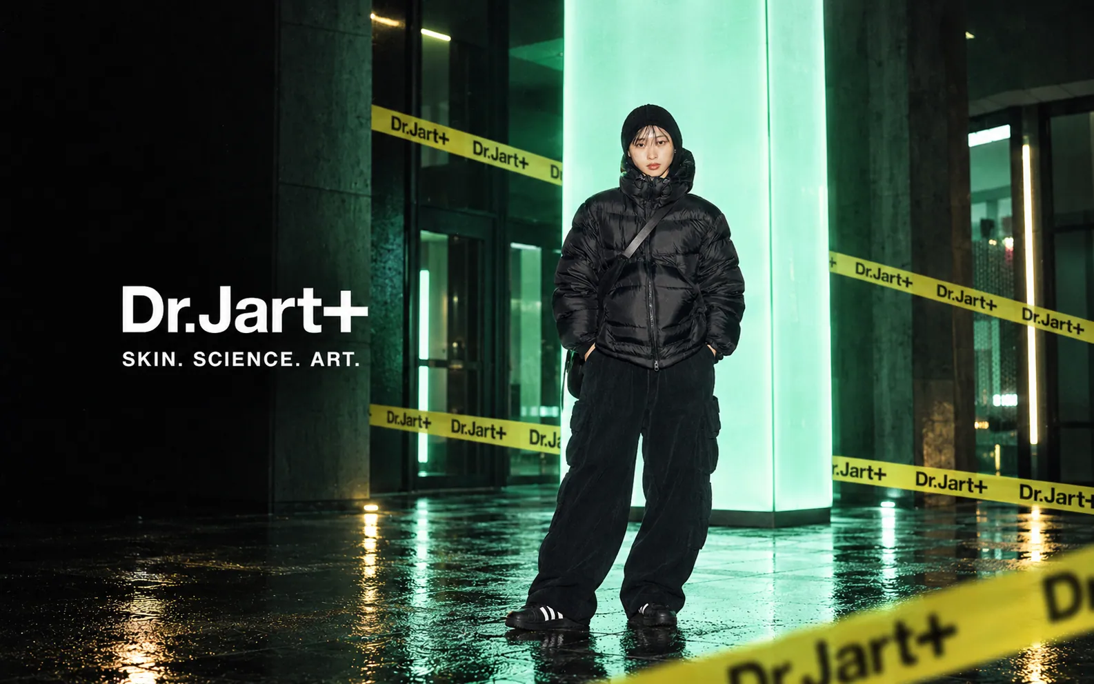 Dr.Jart+ campaign – model in black streetwear in front of a glowing green installation with branded barrier tape