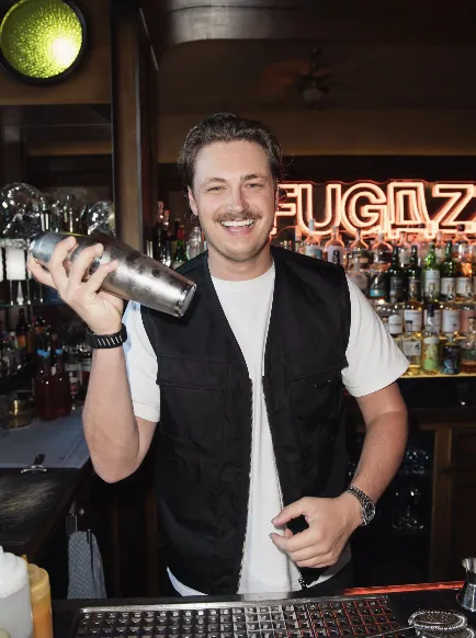 Bartender shaking a cocktail in front of the glowing FUGAZZI neon sign